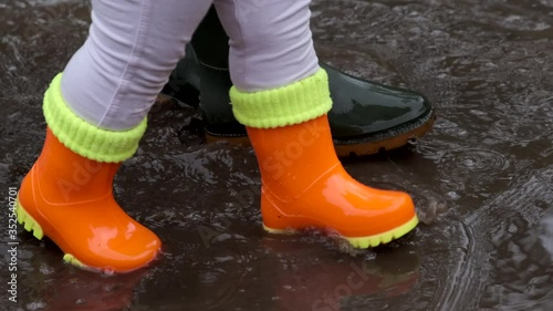 Children and adult rubber boots pass through a puddle.