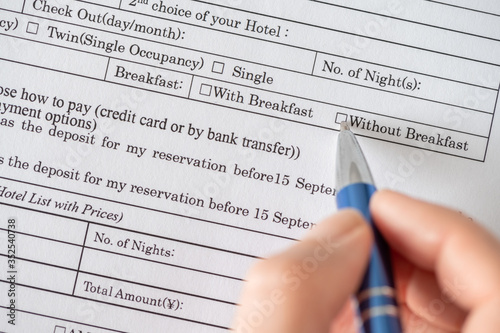 Woman filling hotel reservation form check mark choosing without breakfast in hotel service. Reception desk, registration. Close up. Selective focus.
