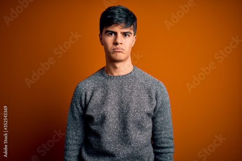 Young handsome man wearing casual sweater standing over isolated orange background depressed and worry for distress, crying angry and afraid. Sad expression. © Krakenimages.com