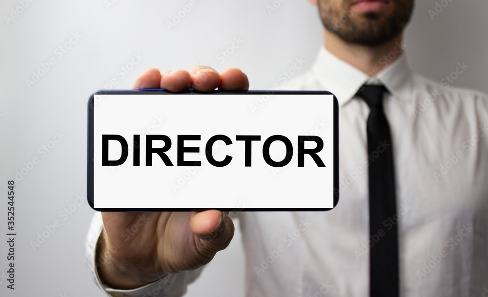 The inscription director on the phone in the hands of a young businessman. A man in a white shirt and tie on the background. The inscription director on the phone in the hands of a young businessman. A man in a white shirt and tie on the background.