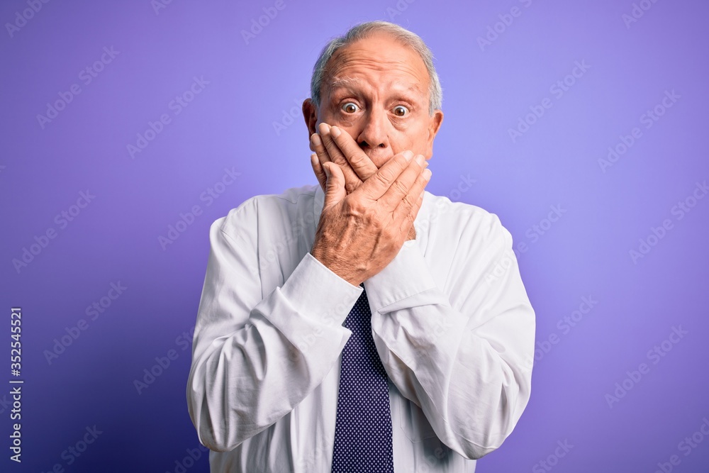Grey haired senior business elegant man standing over purple isolated background shocked covering mouth with hands for mistake. Secret concept.