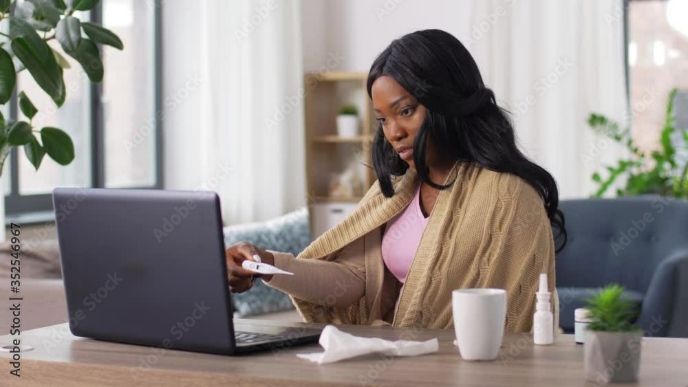 medicine, healthcare and technology concept - sick young african american woman having video call or online consultation on laptop computer and measuring temperature with thermometer at home medicine, healthcare and technology concept - sick young african american woman having video call or online consultation on laptop computer and measuring temperature with thermometer at home