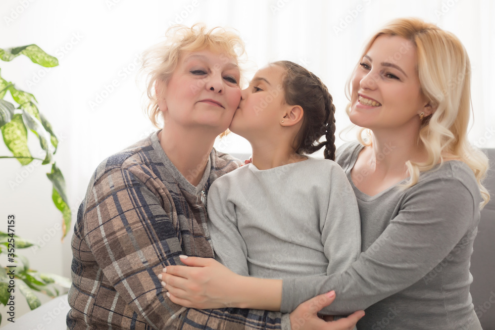 Three generations of women. Beautiful woman and teenage girl are kissing their granny while sitting on couch at home Three generations of women. Beautiful woman and teenage girl are kissing their granny while sitting on couch at home