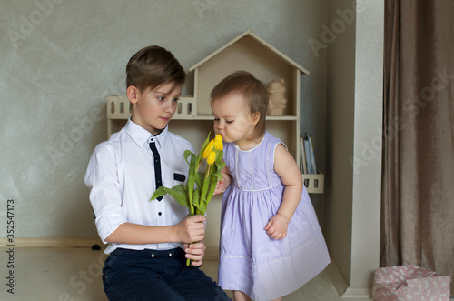Принти на полотні Big brother congratulating his little sister with a bouquet of yellow tulips