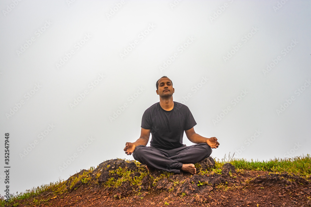 man meditating on rock isolated at the serene nature with white cloud background