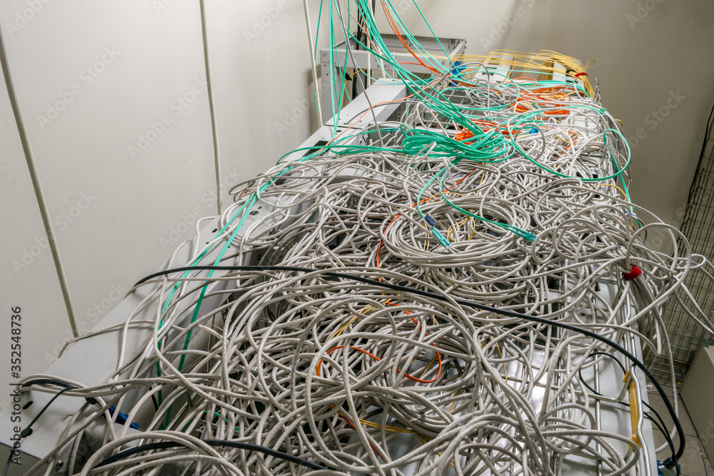Many tangled wires are on top of the server racks of the data center. Internet communication cables are randomly intertwined. Problematic and incorrect wiring.