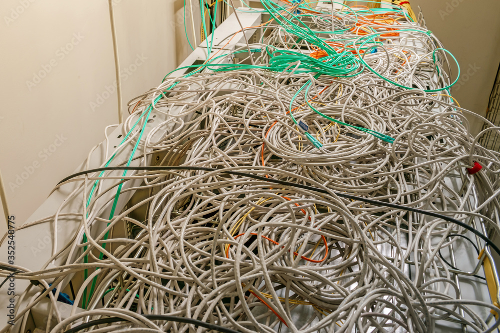 Internet communication cables are randomly intertwined. Problematic and incorrect wiring. Many tangled wires are on top of the server racks of the data center. Internet communication cables are randomly intertwined. Problematic and incorrect wiring. Many tangled wires are on top of the server racks of the data center.