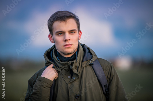portrait of a guy with a backpack on nature against the evening sky	