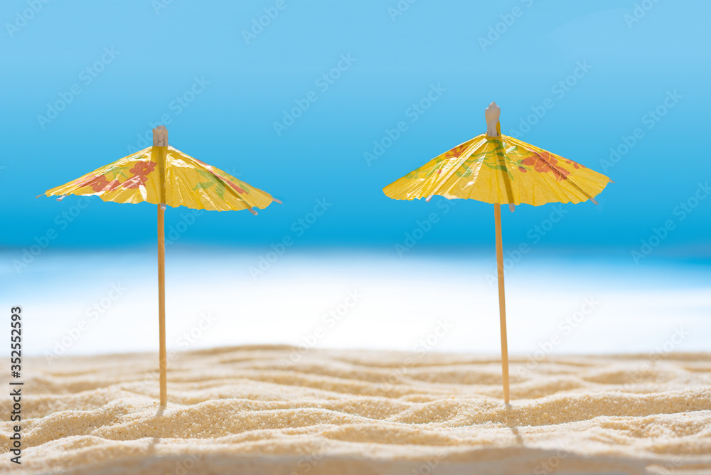 Sun umbrellas on sandy beach with blurry blue ocean and sky. Social distancing or COVID-19 protection at summer holidays. Summer background. Soft focus
