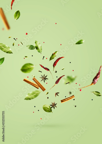 Fototapeta Naklejka Na Ścianę i Meble -  Flying spices bay leaf, red chili pepper, anise, cinnamon sticks on a green background.