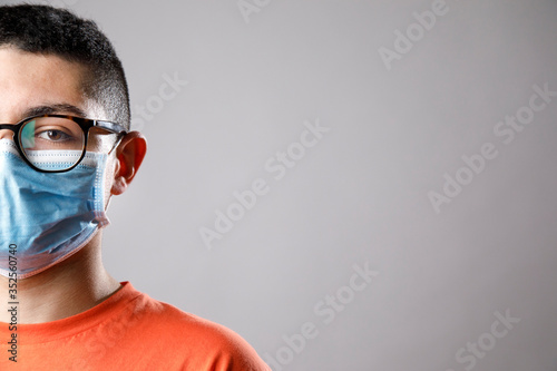 Ritratto di ragazzo giovane con occhiali da vista , maglia arancione e mascherina chirurgica , isolato su sfondo grigio photo