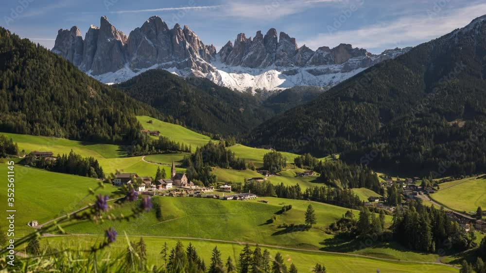 Time lapse of clouds moving over The Dolomites mountain peaks on a sunny day with green rolling hills below and a town surrounded by pine trees in St Magdalena, Northern Italy.
Time lapse of clouds moving over The Dolomites mountain peaks on a sunny day with green rolling hills below and a town surrounded by pine trees in St Magdalena, Northern Italy.