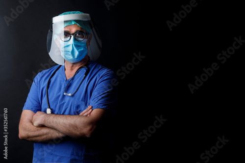 Medico  con protezioni mascherina chirurgica , visiera in plastica e camice blu isolato su sfondo nero photo