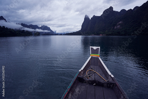 Traditional wooden boat with water, sky and rocks in Cheow Lan Lake, Khao sok national park, Thailand.