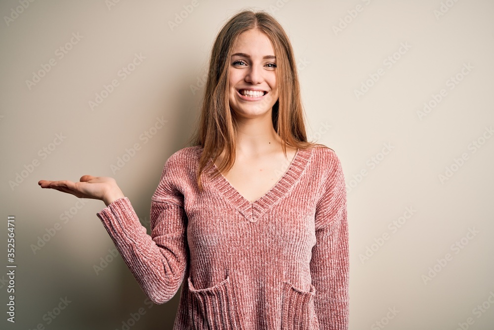 Young beautiful redhead woman wearing pink casual sweater over isolated white background smiling cheerful presenting and pointing with palm of hand looking at the camera. Young beautiful redhead woman wearing pink casual sweater over isolated white background smiling cheerful presenting and pointing with palm of hand looking at the camera.