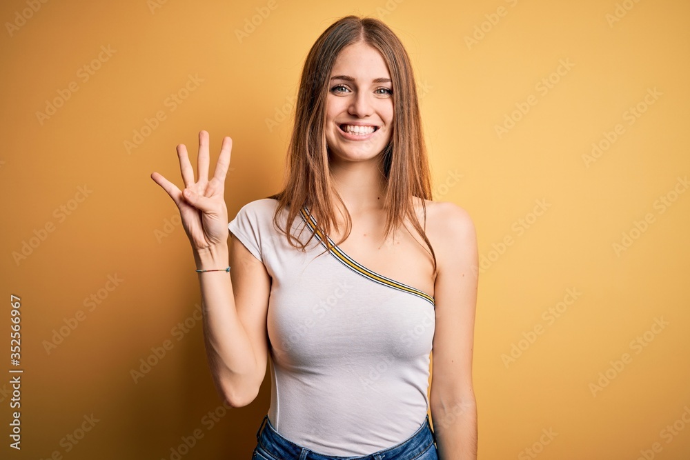 Young beautiful redhead woman wearing casual t-shirt over isolated yellow background showing and pointing up with fingers number four while smiling confident and happy. Young beautiful redhead woman wearing casual t-shirt over isolated yellow background showing and pointing up with fingers number four while smiling confident and happy.