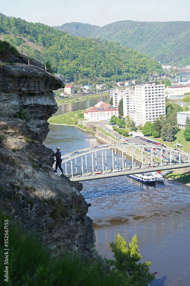 Fototapeta premium Woman climbing difficult steep wall above river and town, via ferrata route, Shepherd's Wall, Decin, Czech Republic