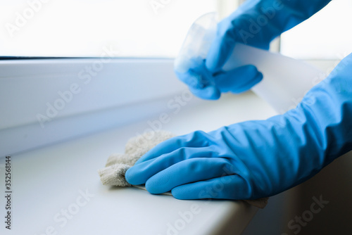 Cleaning windowsill surface with spray in protective gloves
