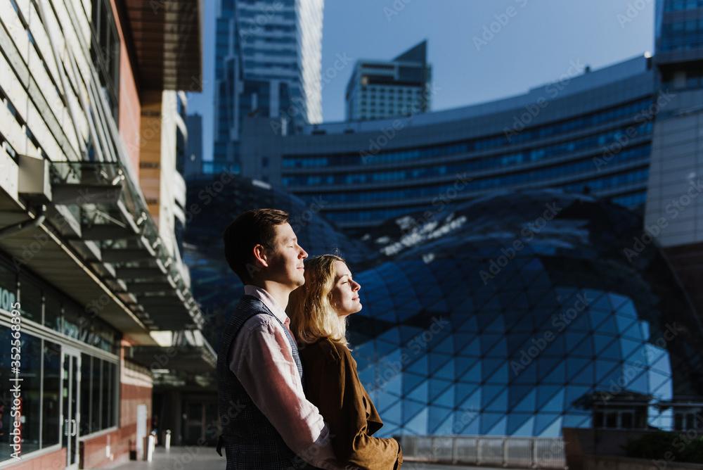 Fototapeta premium A young woman and a man hug, kiss and walk in the city center near skyscrapers.