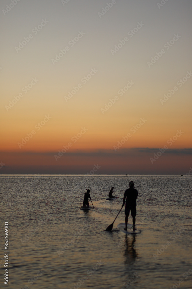 People on sup-boards meet sunrise at the sea. Silhouettes of people on sap boards.