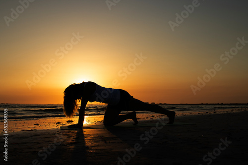 silhouette of woman practicing yoga on the beach at sunset