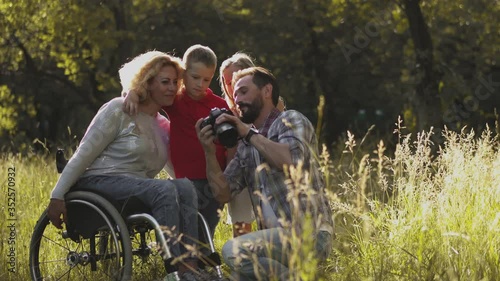 The father photographs the family with a professional camera. Family with a disabled mom in a wheelchair take a family photo with children in nature. Family concept. Toned footage. Prores 422. 