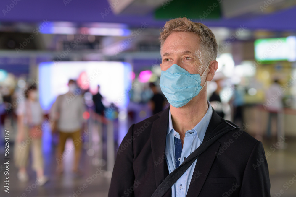 Mature businessman with mask walking off the sky train station Mature businessman with mask walking off the sky train station