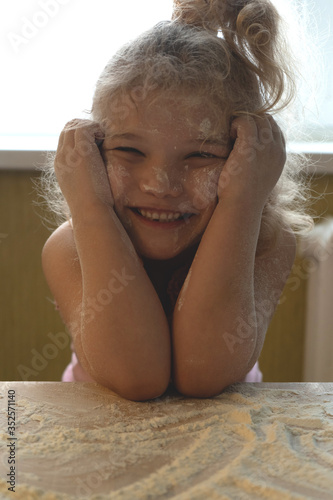 a little girl smiles and plays with white flour