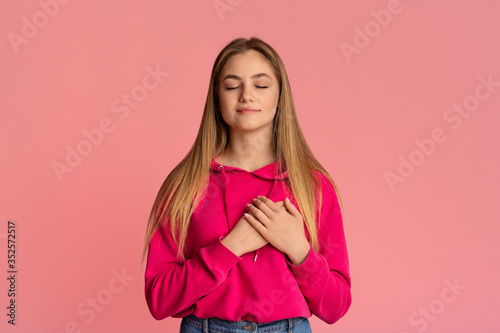 Cute girl tenager with closed eyes presses her hands to heart photo