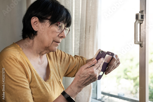 Old woman looking the smart phone in the window
