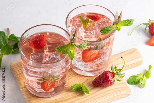 Fresh aromatic strawberry lemonade with ice cubes and mint on the wooden tray close up. Summer refreshing drink on the table.