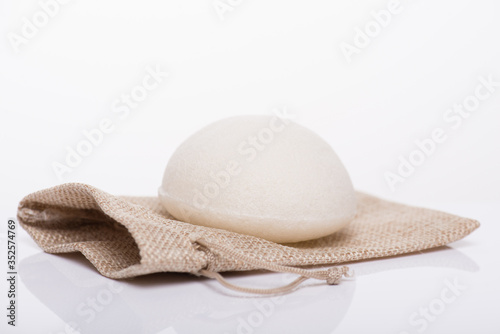 Close-up photo of white konjac sponge without additives lying on craft small case package bag isolated on white background photo