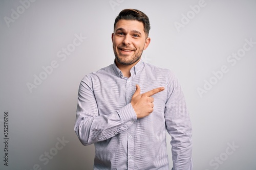 Young business man with blue eyes standing over isolated background cheerful with a smile of face pointing with hand and finger up to the side with happy and natural expression on face