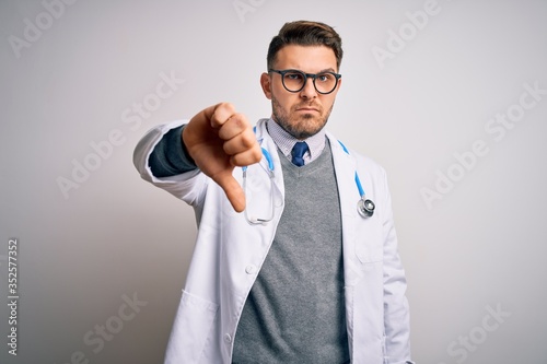 Young doctor man with blue eyes wearing medical coat and stethoscope over isolated background looking unhappy and angry showing rejection and negative with thumbs down gesture. Bad expression. © Krakenimages.com
