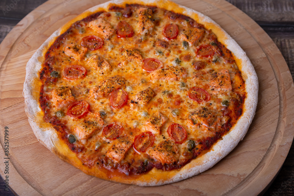 Pizza with salmon, tomatoes and capers on a wooden board. Whole pizza. Close-up.