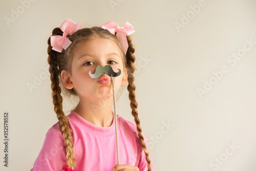A little girl with pigtails tries on a festive mustache.