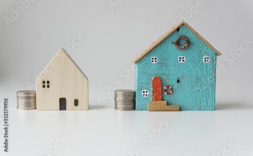 2 small blue and white houses with coins stacked beside the house, on white background, saving ideas for the future.