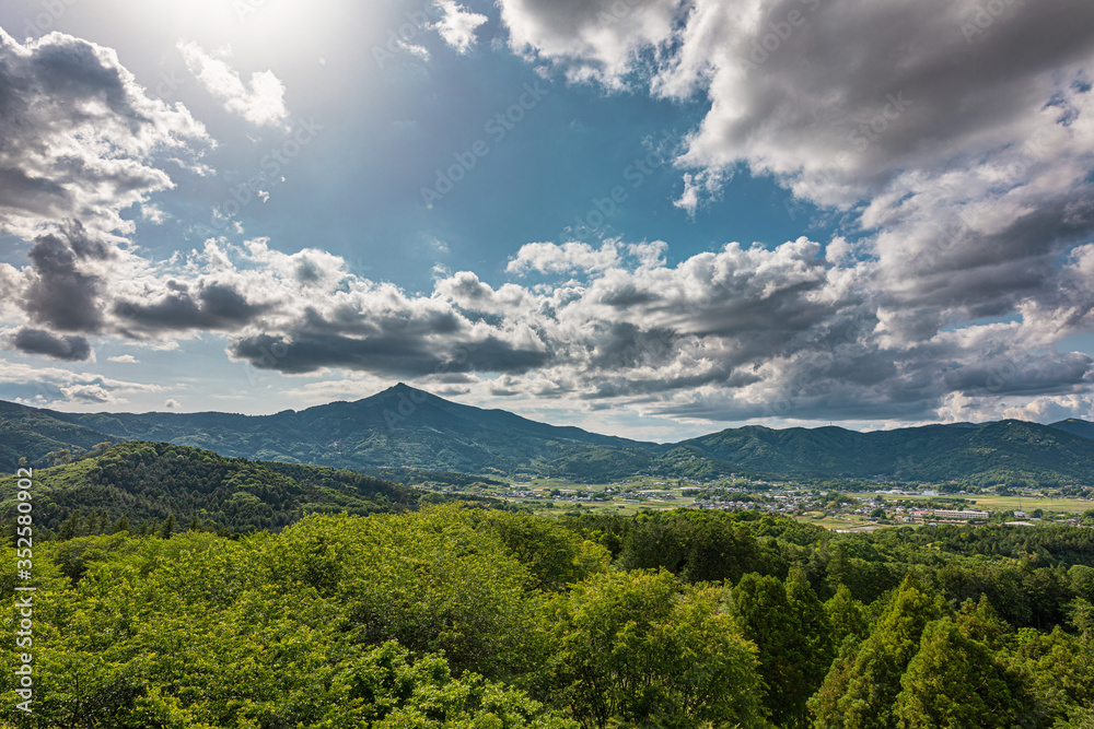 太陽光に照らされた大きな雲と新緑の里山