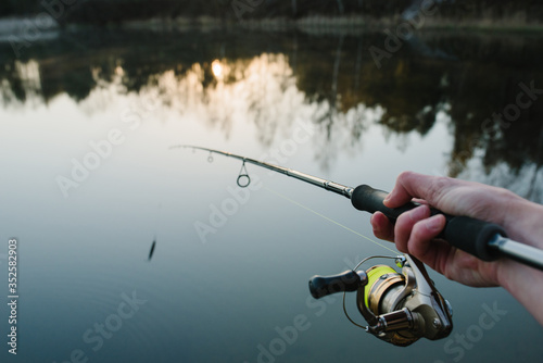 Fisherman with rod throws bait into water on river bank. Fishing for pike, perch. Background wild nature. Concept of rural getaway. Man catching a fish on lake or pond with text space. Fishing day