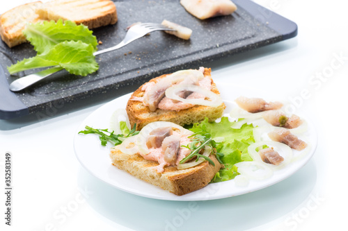 sandwich with salad, herring and herbs with onions in a plate