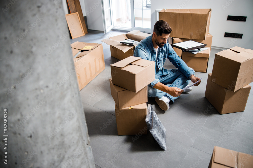 Fototapeta premium Young bearded man arranging things after moving to new flat