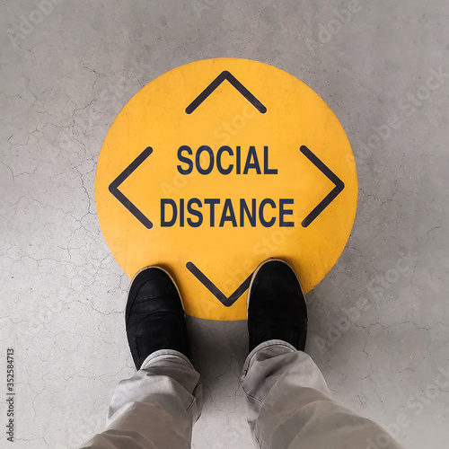 A person standing on a social distancing sign photo