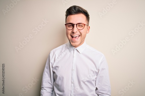 Young handsome business mas wearing glasses and elegant shirt over isolated background winking looking at the camera with sexy expression, cheerful and happy face.