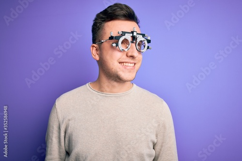 Young handsome caucasian man wearing optometrical glasses over purple background looking away to side with smile on face, natural expression. Laughing confident. © Krakenimages.com