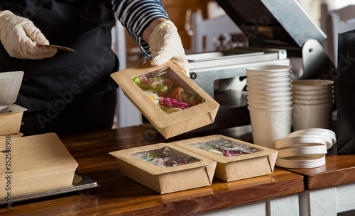 Restaurant worker wearing protective mask and gloves packing food boxed take away. Food delivery services and Online contactless food shopping. photo