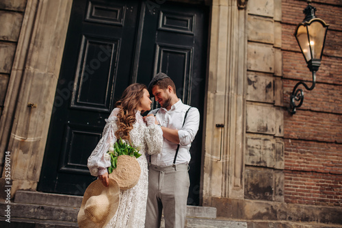 The groom gently embraces the beauty bride under a streetlight near an old building . he kisses his on the forehead.