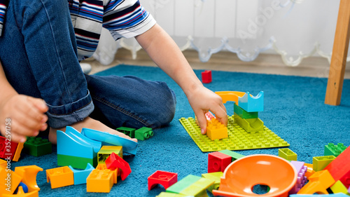 Closeup image of little boy assembling colorful toy constructor on carpet