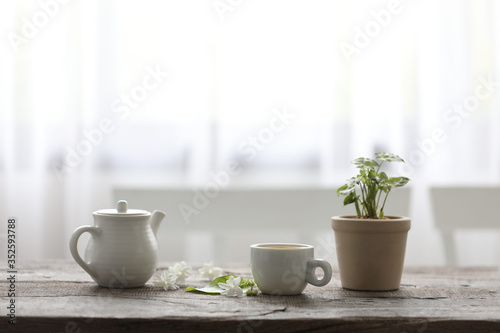 White tea cup and tea pot with plant on wooden table minimal interior  