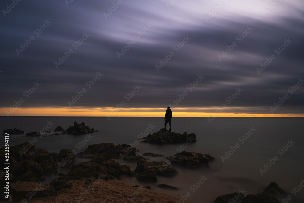 silueta de un hombre parado entre las rocas del mar mediterráneo durante el atardecer