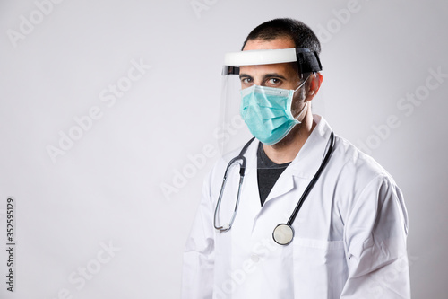 medico con camice bianco e mascherina chirurgica indossa uno schermo di protezione in plexligass, isolato su sfondo bianco photo